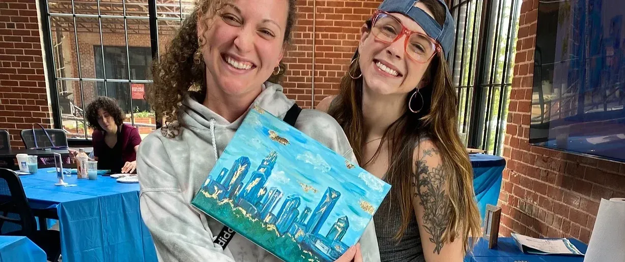 Two smiling students holding a gilded skyline painting