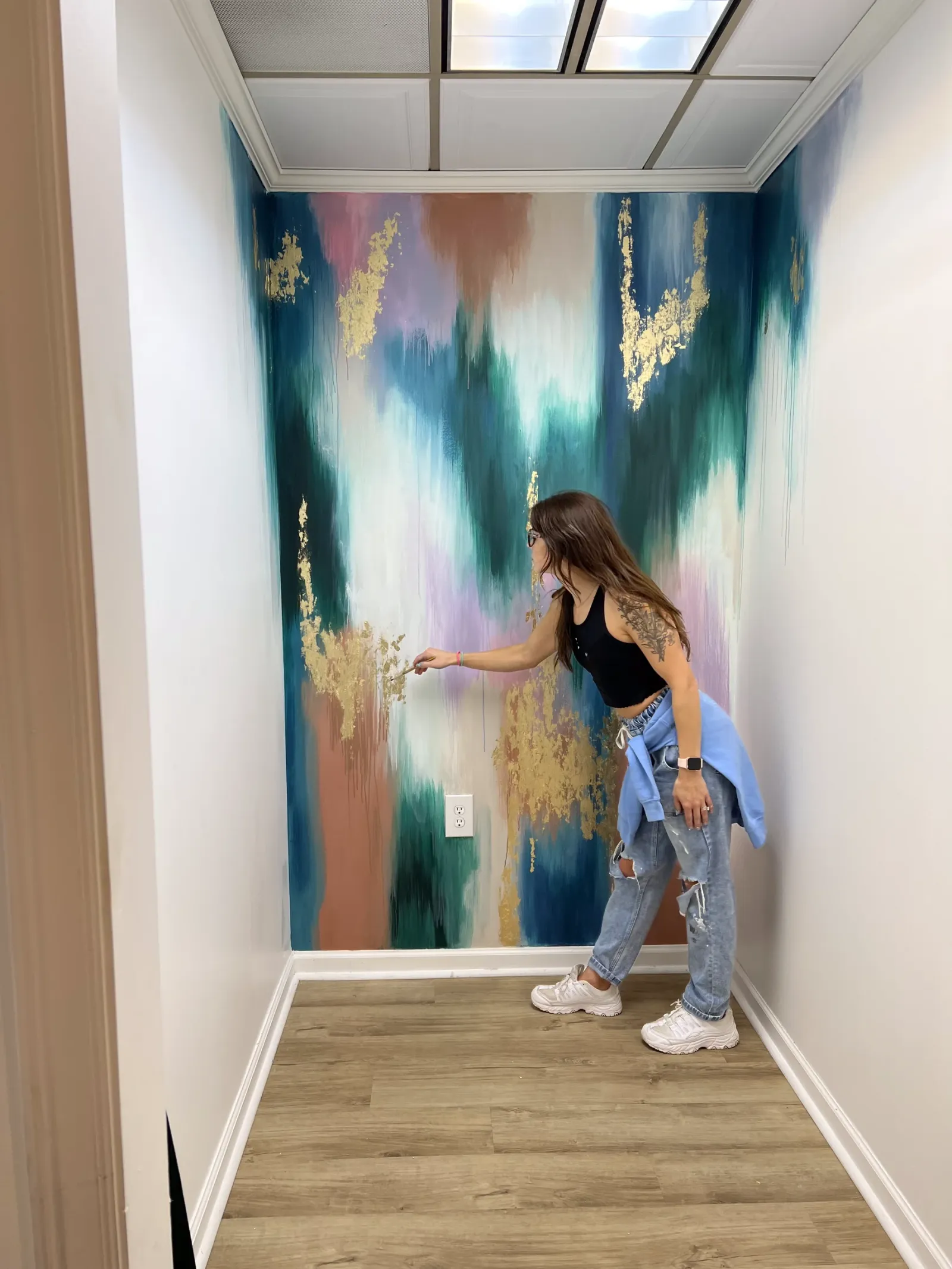 Kelly adding gold leaf to a teal and blush alcove mural