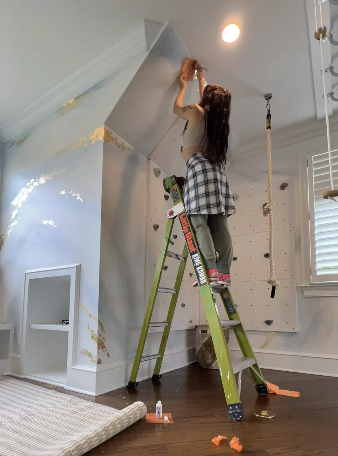 Kelly on a ladder gilding a white wall