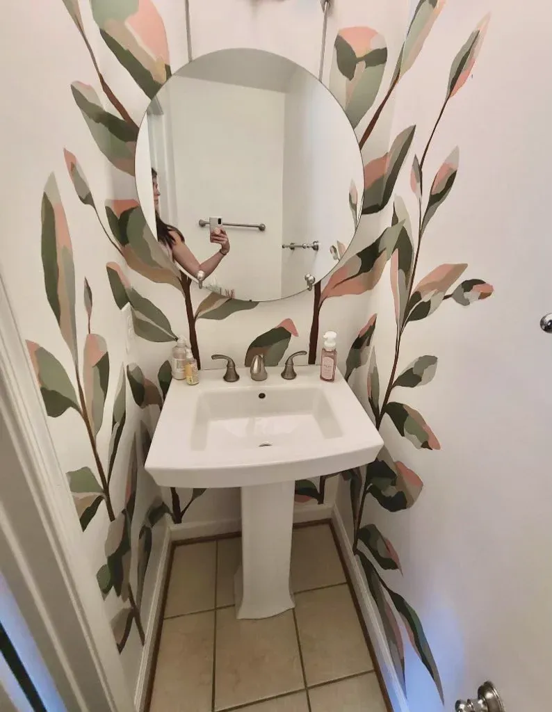 Painted green and blush leaves climbing around a powder room mirror