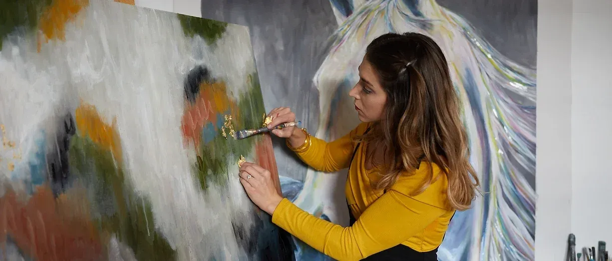 Kelly Aiken pressing gold leaf onto an abstract canvas in her studio